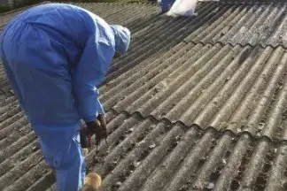 Worker in blue protective clothing lifting corrugated roof sheeting